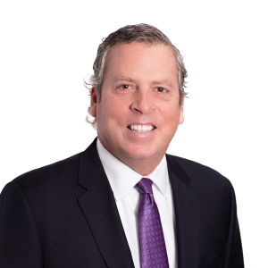 A smiling individual wearing a suit with a purple tie and white shirt.
