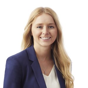 A smiling woman wearing a blue blazer over a white top with a small pendant necklace.