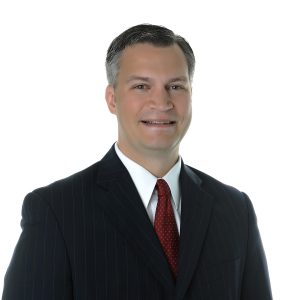 A smiling person in professional attire with a tie against a white background.
