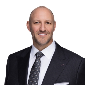 A smiling person wearing a suit with a blue tie against a white background.