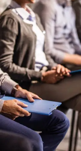 A row of individuals sits while holding folders or engaging with their phones.