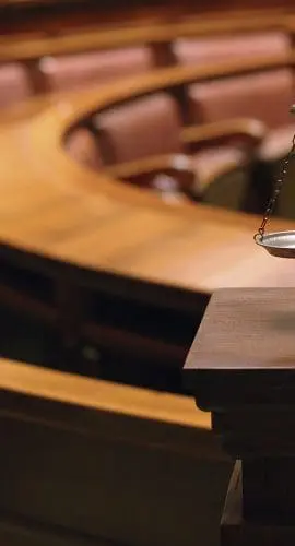 A set of balanced scales sits on a pedestal in an empty courtroom.