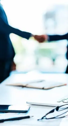 Cropped shot of a laptop on a desk with two businesspeople shaking hands in the background
