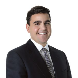 A person is smiling and wearing a business suit with a tie.