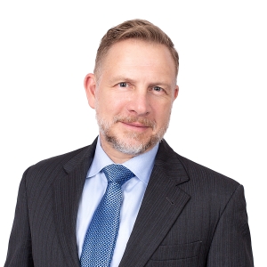 A person wearing a suit with a red tie poses against a white background.