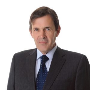 A formally dressed person with a tie is posing for a professional headshot against a plain background.