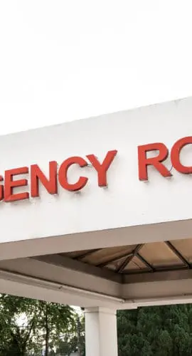 Sign for an emergency room entrance with trees and buildings in the background.