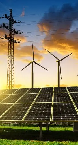 Solar panels and wind turbines are positioned against a backdrop of a dramatic sunset sky, illustrating a clean energy concept.