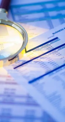 A magnifying glass lies over financial documents next to a calculator, highlighting the concept of financial analysis or audit.