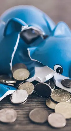 A shattered blue piggy bank with coins scattered around it on a wooden surface.