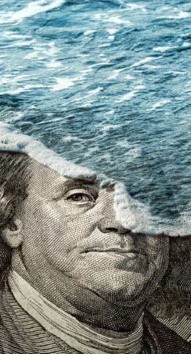 A hundred-dollar bill partially submerged under waves of ocean water.