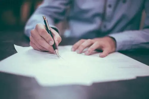 A person filling out paperwork at desk, neck down
