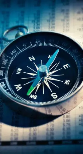 A compass is lying on top of financial documents with numerical data.