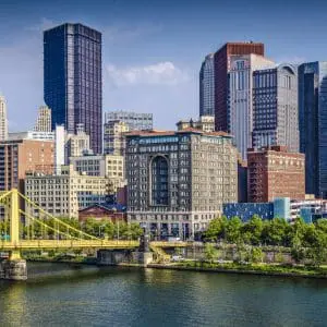 A vibrant cityscape with skyscrapers, a bridge across a river, and clear blue skies.
