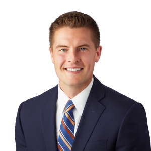 A person is smiling and dressed in professional attire with a blue suit and a striped tie.