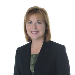 A smiling individual with short hair wearing a black blazer over a green top against a white background.