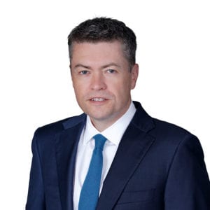 A person in a suit and tie is shown against a plain white background.