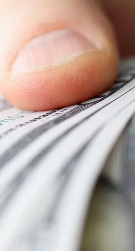 A hand is holding a fanned-out stack of US dollar bills.