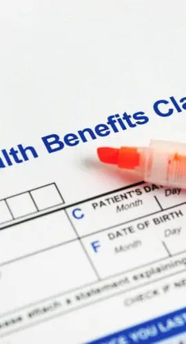 A health benefits claim form is partially filled out with a pen resting on top.
