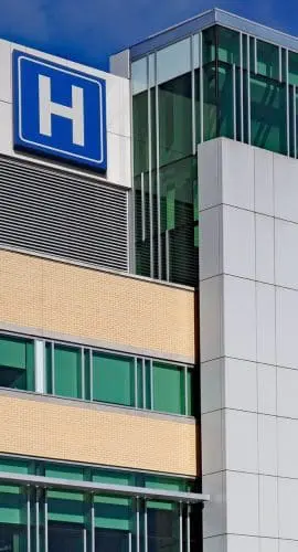 A modern hospital building with a large blue "H" sign indicating it is a medical facility.