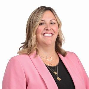 A person wearing a pink blazer and smiling against a white background.