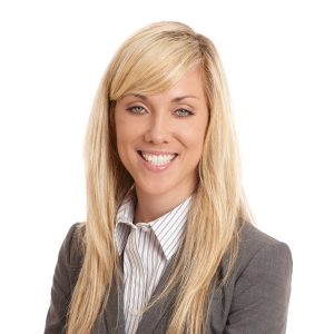 A smiling person with blond hair wearing a professional business suit and striped shirt.
