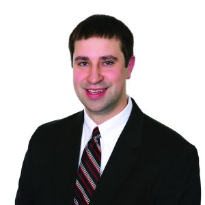A smiling individual dressed in professional attire with a suit and striped tie against a white background.