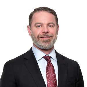 A man with a beard is wearing a suit and tie against a white background.