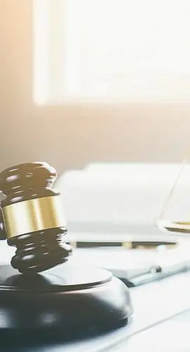 A judge's gavel and a balance scale are presented on a desk, illuminated by natural light, suggesting a legal or judicial setting.