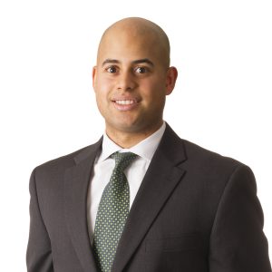 A man in a suit with a green tie is smiling against a white background.