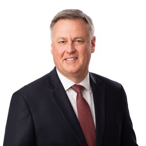 A man in a business suit with a red tie smiles for a portrait.