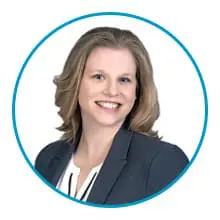 A professional individual smiles, wearing a dark blazer and a white top with a striped pattern, set within a blue circular frame.