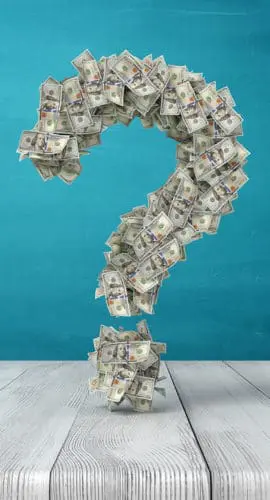 A question mark made of dollar bills stands on a wooden surface against a blue background.