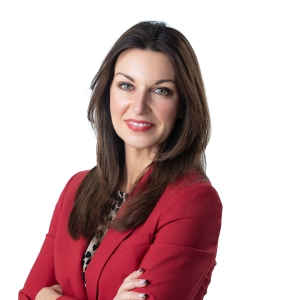 A woman with long dark hair is wearing a red blazer over a leopard print blouse and smiling at the camera.