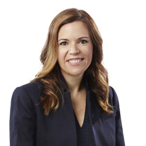 A smiling woman with shoulder-length brown hair wearing a dark blue blazer over a patterned top.