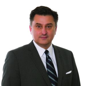 A man in a pinstripe suit and striped tie stands against a white background.