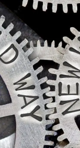 Interlocking metal gears with the words "OLD WAY" and "NEW WAY" engraved on them, symbolizing change and progression.
