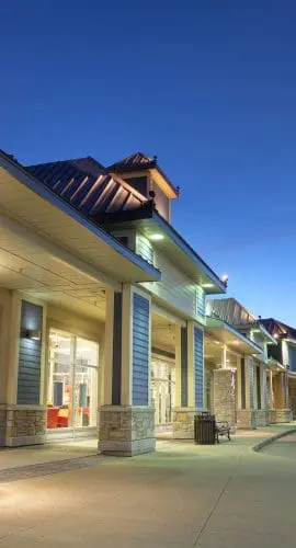 A row of illuminated storefronts under a dusk sky.