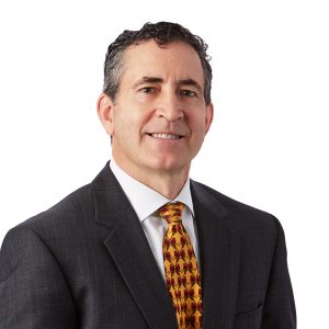A person in professional attire with a patterned tie is posing for a portrait against a plain background.
