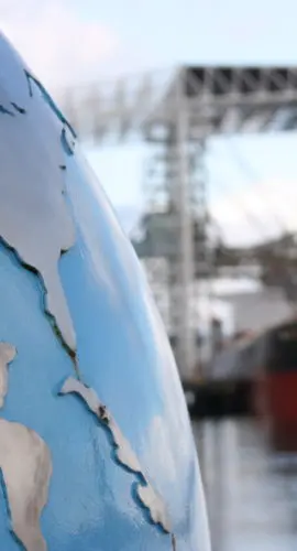 A globe with focus on the United States (USA) and Central America contrsted against a blurred background of a bulk cargo ship exemplifying the global nature of the cargo industry. Look at more