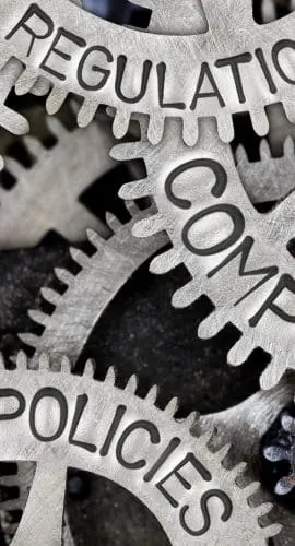 A network of metal gears is inscribed with the words "RULES," "REGULATIONS," "STANDARDS," "POLICIES," and "COMPLIANCE."