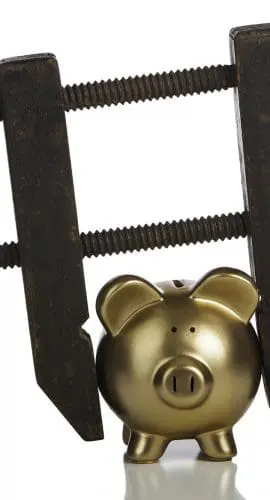 A gold piggy bank is being squeezed by a carpenter's vise with wooden handles.
