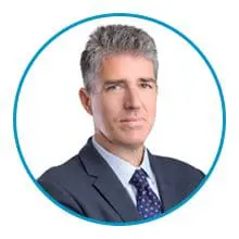 A man with short gray hair is wearing a suit and tie inside a blue circle frame.