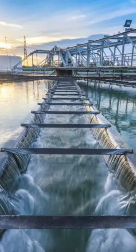 A water treatment plant with cascading flows and a structural metal framework against a backdrop of a setting sun and clear skies.