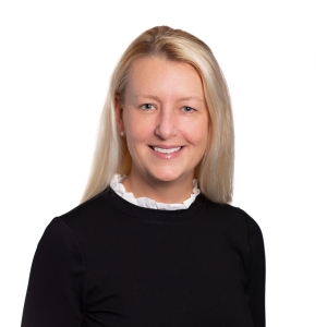A smiling woman with blond hair, wearing a black top with a white collar, poses for a professional portrait.