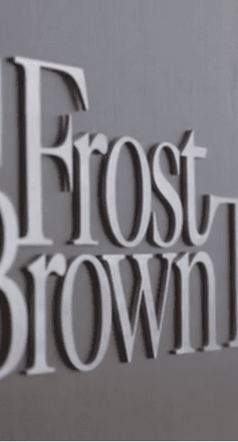 A metallic wall sign of "Frost Brown Todd LLC" with a shadow being cast on the wall.